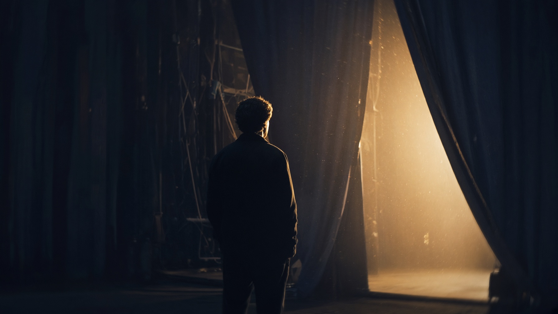 James Barbour standing backstage in the wings, silhouetted against warm stage light before a Broadway performance